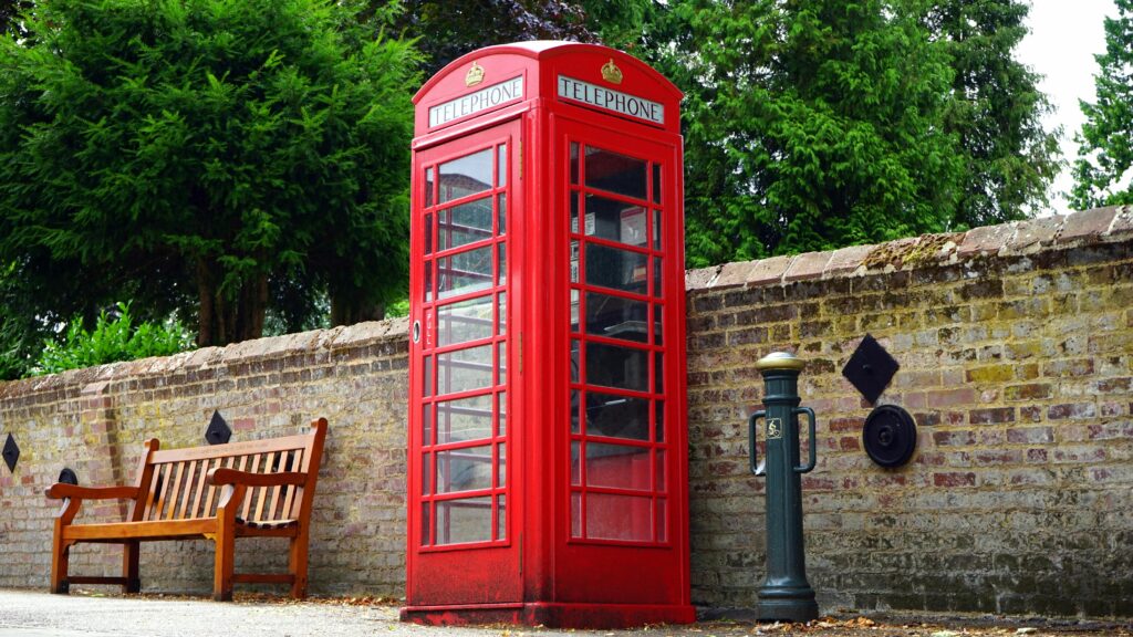 A vintage red telephone booth beside a brick wall, symbolizing British culture.